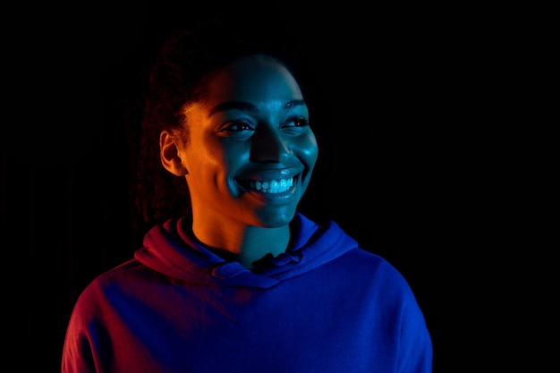 Portret van een jonge afro-amerikaanse vrouw die zich voordeed en glimlachte geïsoleerd op een donkere achtergrond in veelkleurig neonlicht