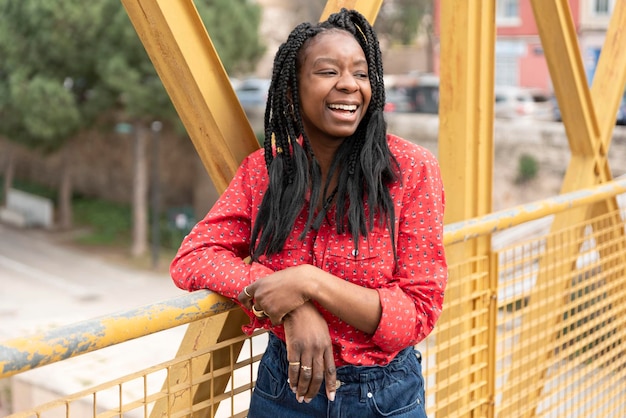 Portret van een jonge afro-amerikaanse vrouw in vlechten leunend op een gele brug lachend