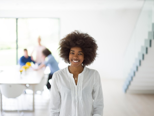 portret van een jonge Afro-Amerikaanse zakenvrouw bij een modern opstartend kantoorinterieur, team in vergadering op de achtergrond