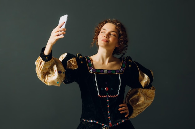 Portret van een jonge aristocratische vrouw die een selfie maakt met een mobiele telefoon en gekleed in een middeleeuwse jurk