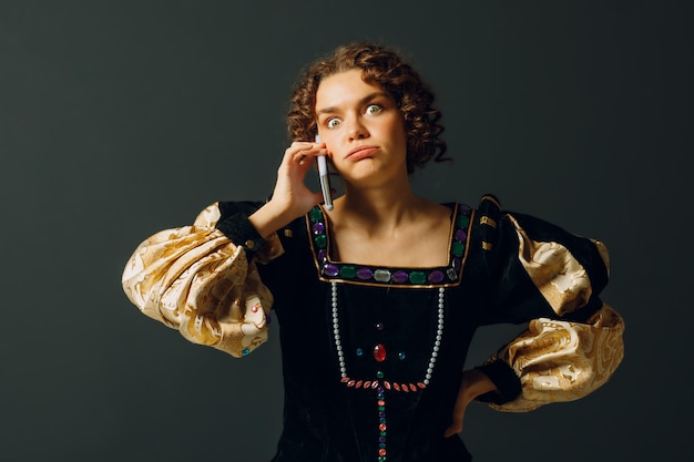 Portret van een jonge aristocratische vrouw die op een mobiele telefoon praat, gekleed in een middeleeuwse jurk in het donker