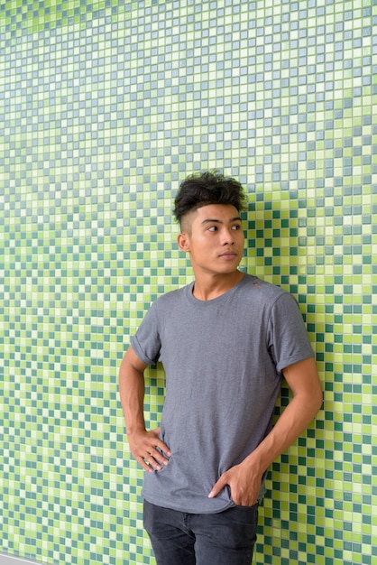 Portret van een jonge Aziatische man met krullend haar op groen betegelde muur