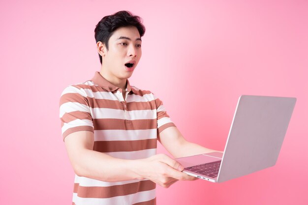 Portret van een jonge Aziatische man met laptop op roze achtergrond