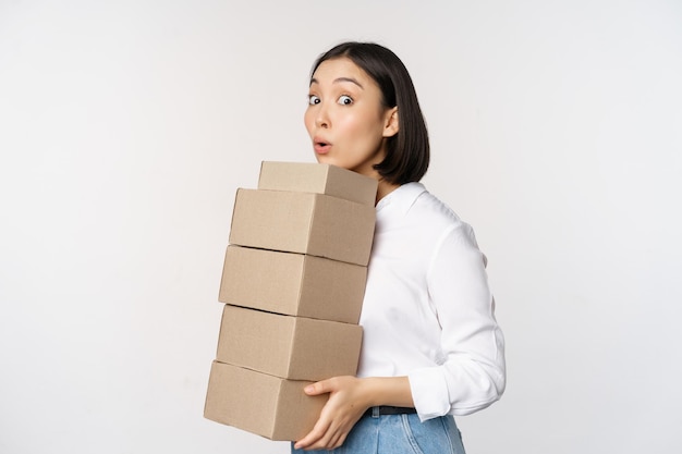 Portret van een jonge aziatische vrouw die dozen vasthoudt en leveringsgoederen draagt. Koreaanse vrouwelijke ondernemer verzamelt bestelling staande voer witte achtergrond