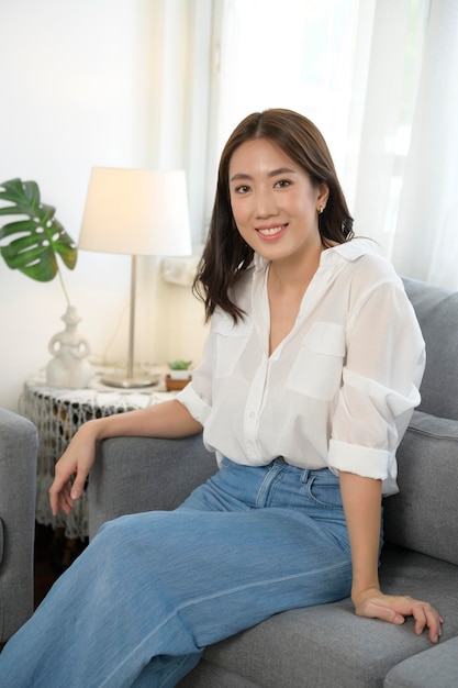 Portret van een jonge Aziatische vrouw die lacht op de bank in de woonkamer