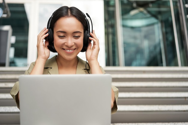 Portret van een jonge aziatische vrouw die met een laptop en een koptelefoon naar video kijkt, doet online cursus o