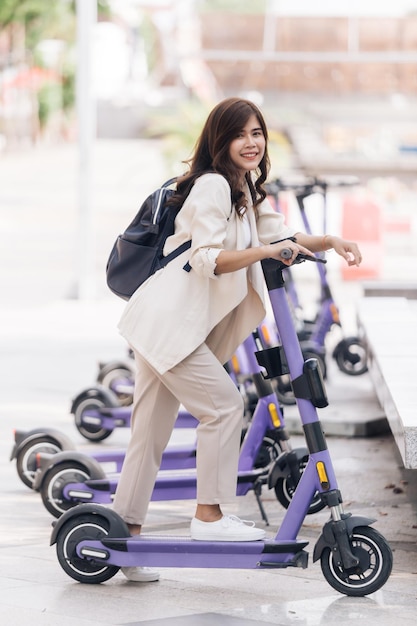 Portret van een jonge Aziatische vrouw die op een elektrische scooter in het park rijdt