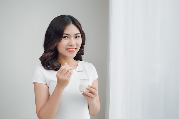 Portret van een jonge aziatische vrouw die thuis yoghurt eet eating