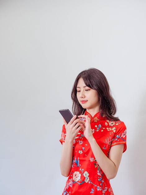 Portret van een jonge aziatische vrouw die traditionele cheongsam qipao-jurk draagt met smartphone op witte achtergrond