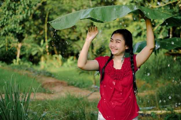 Portret van een jonge Aziatische vrouw zat onder een bananenblad en zocht beschutting tegen de regen op de achtergrond van de groene tuin