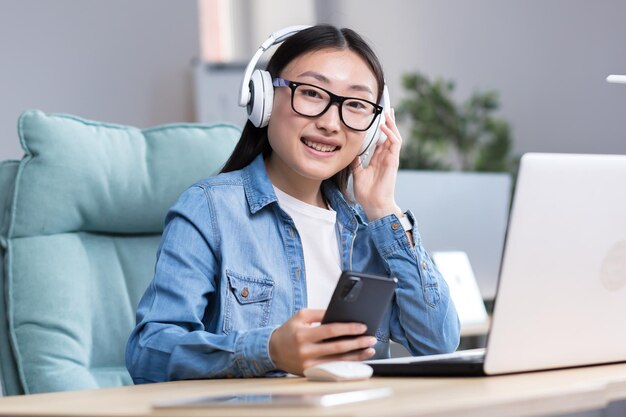 Portret van een jonge Aziatische vrouwelijke student die online studeert op een laptop met een laptop en een koptelefoon om