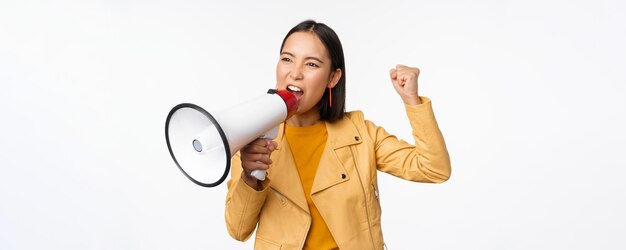 Portret van een jonge aziatische vrouwendemonstrant die schreeuwt in een megafoon en protesteert terwijl hij vol vertrouwen staat