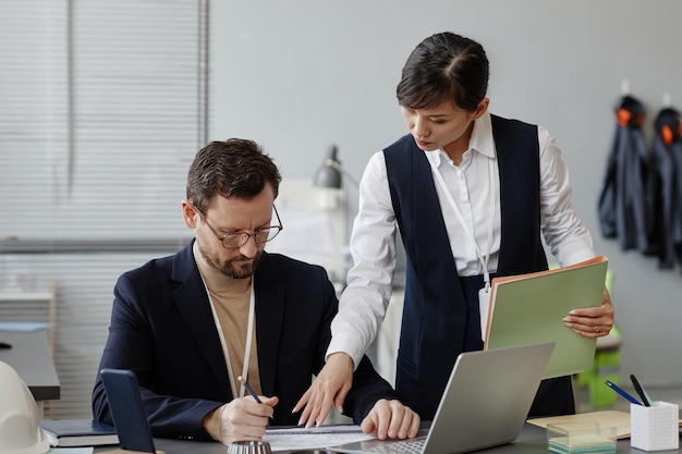 Portret van een jonge Aziatische zakenvrouw die een ingenieur op de werkplek in het kantoor instrueert