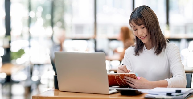 Portret van een jonge Aziatische zakenvrouw die werkt op een laptopcomputer die aan een bureau zit