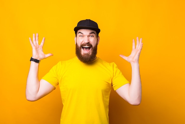 Foto portret van een jonge bebaarde hipster man verrast gebaar maken over gele muur