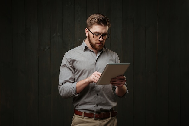 Portret van een jonge, bebaarde man in brillen met behulp van tabletcomputer geïsoleerd op een zwarte houten ondergrond