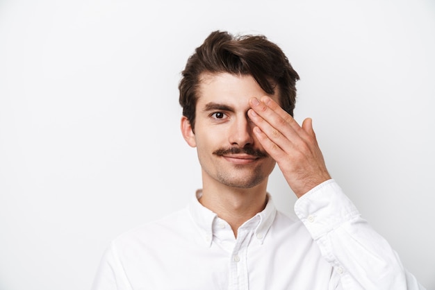 Portret van een jonge besnorde man die overhemd draagt dat aan voorzijde kijkt en zijn die oog coning op wit wordt geïsoleerd