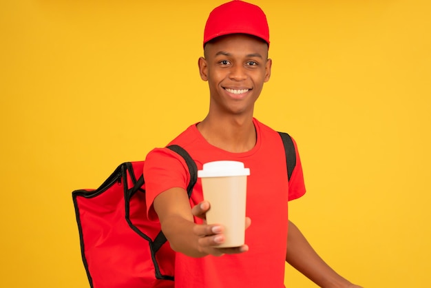 Portret van een jonge bezorger met een kopje afhaalkoffie. Levering dienstverleningsconcept.