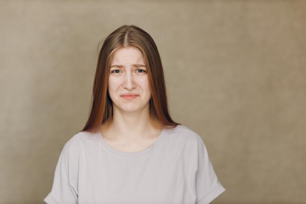 Portret van een jonge blanke actrice die van streek is en naar de camera kijkt tegen een beige achtergrond Acteertest