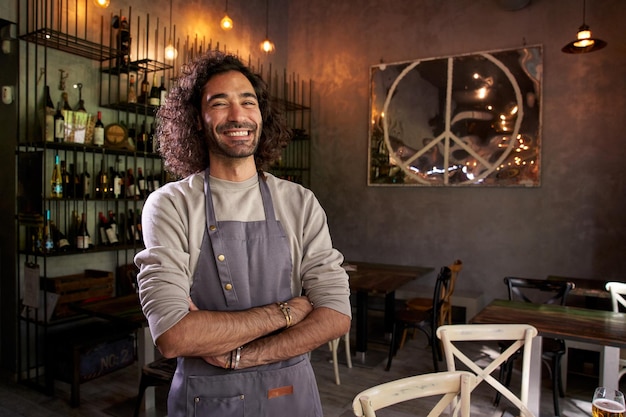 Portret van een jonge blanke man die naar de camera kijkt in een restaurant met een trotse en glimlachende ober