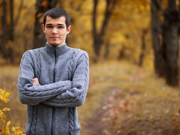 Portret van een jonge blanke man in een gebreide wollen warme trui in het najaar park