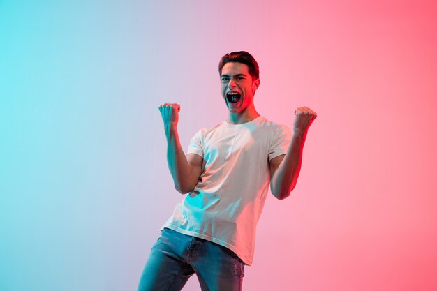 Portret van een jonge blanke man op blauw-roze studioachtergrond met kleurovergang in neonlicht