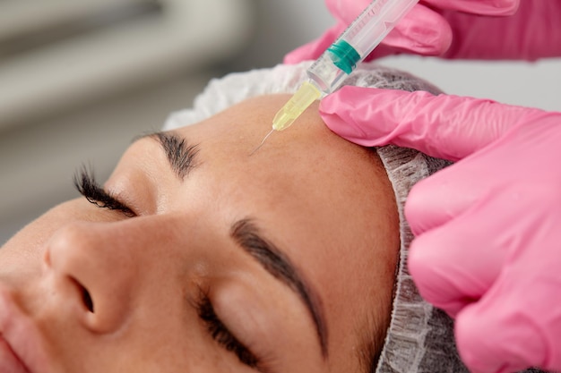 Portret van een jonge blanke vrouw die cosmetische botox-injectie in voorhoofd krijgt Mooie vrouw krijgt botox-injectie in haar gezicht