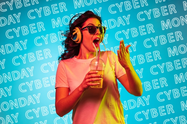 Portret van een jonge blanke vrouw in koptelefoon en zonnebril op blauwe achtergrond met neonletters. Concept van verkoop, zwarte vrijdag, cybermaandag, financiën, zaken. Online winkels en betalingen factuur.