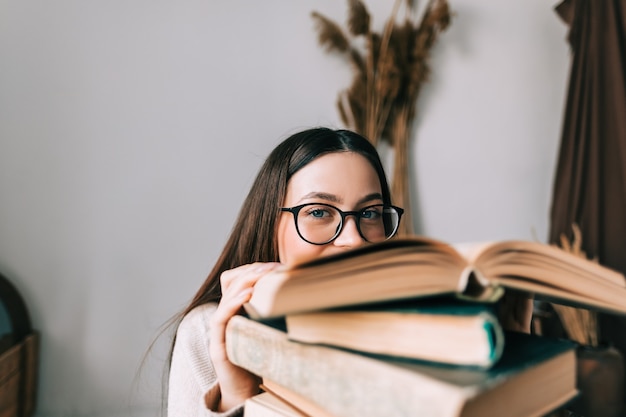 Portret van een jonge blanke vrouw student in oogglazen verstopt achter een boek