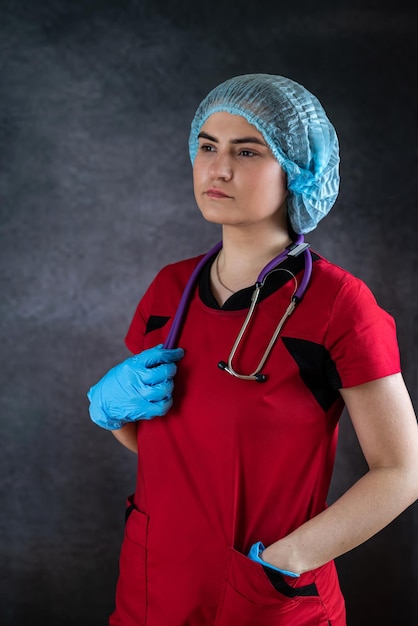 Portret van een jonge blanke vrouwelijke verpleegster of arts die rode uniforme blauwe handschoenen met stethoscoop draagt