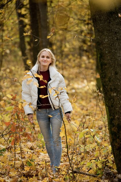 Portret van een jonge blonde vrouw in het herfstbos, met een boeket gele bladeren in haar handen.