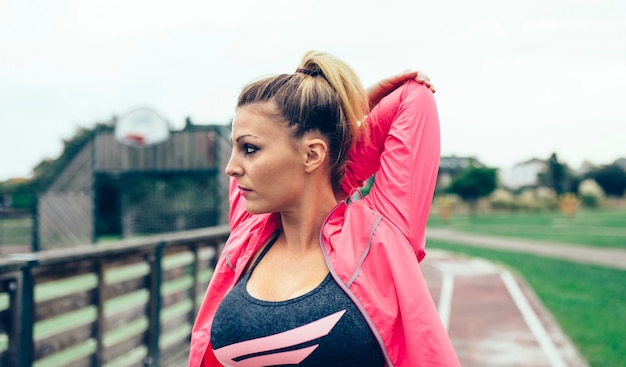 Portret van een jonge blonde vrouw met een staart die de armen uitrekt voordat ze buiten gaat trainen