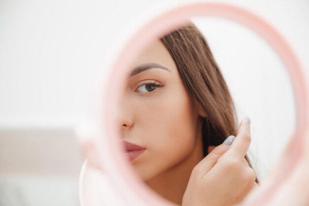 Portret van een jonge brunette die in de spiegel kijkt de weerspiegeling van een vrouw in de spiegel het meisje bewondert haar weerspiegeling in de spiegel