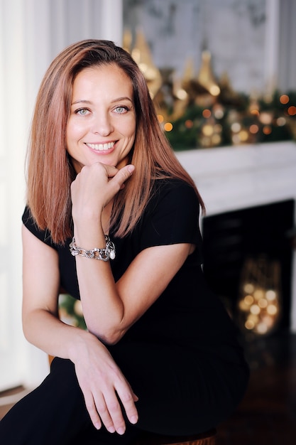 Portret van een jonge brunette meid met een mooie glimlach, lang haar in zwarte kleding in de buurt van de kerstboom