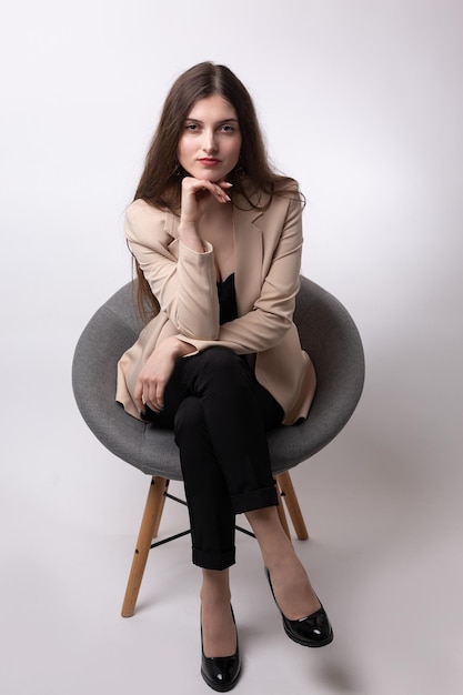 Portret van een jonge brunette met lang haar in de studio Leuk meisje zittend op een stoel op een witte achtergrond