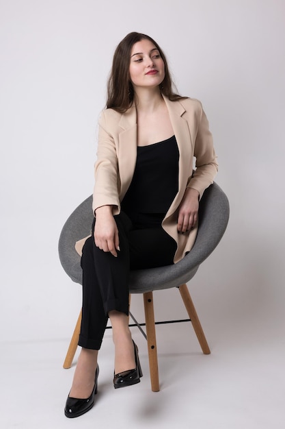 Portret van een jonge brunette met lang haar in de studio Leuk meisje zittend op een stoel op een witte achtergrond