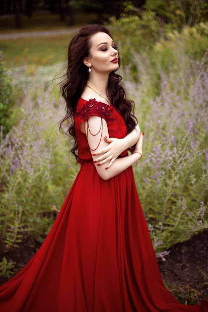 Portret van een jonge brunette vrouw in een rode jurk met een trein