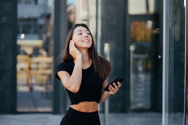 Portret van een jonge brunette vrouw met koptelefoon en lachend tijdens het wandelen