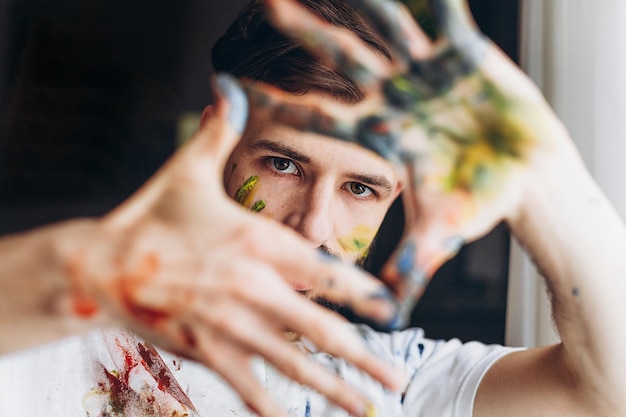 Foto portret van een jonge creatieve kunstenaar die een wit t-shirt draagt met gekleurde vlekken van verf die poseert voor een foto tijdens het maken van een foto