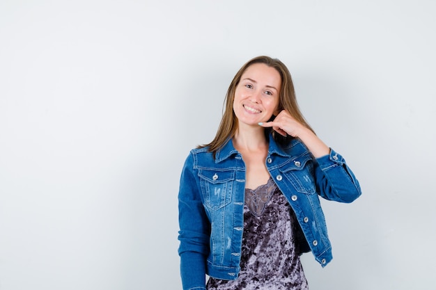 Portret van een jonge dame met telefoongebaar in blouse, spijkerjasje en zelfverzekerd vooraanzicht