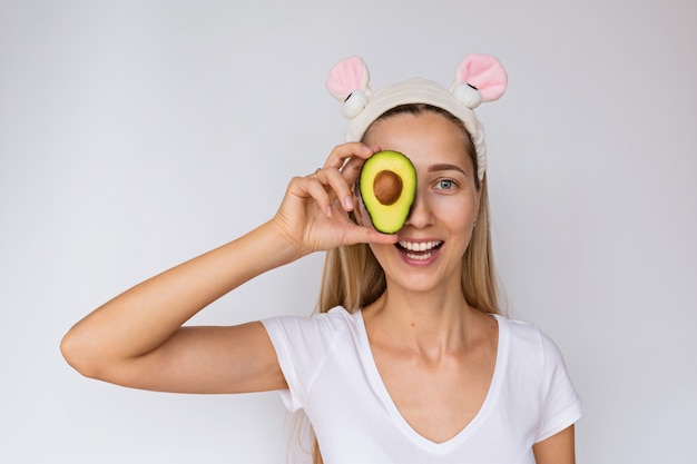 Portret van een jonge de hand verse avocado van de vrouwenholding dichtbij haar gezicht op wit.