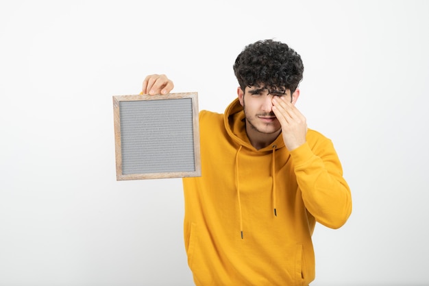 Portret van een jonge donkerbruine mens die grijs frame bevindt zich houdt.