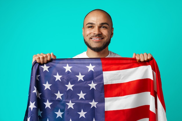 Portret van een jonge donkere man die trots de vlag van de VS op turkoois houdt