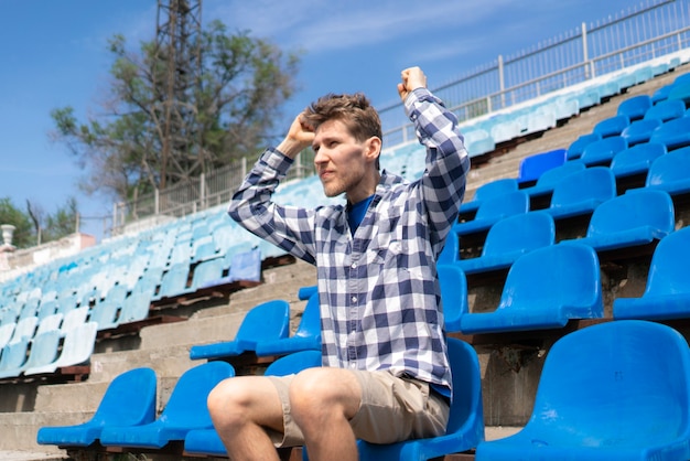 Portret van een jonge emotionele man die tijdens wedstrijdevenementen op het sportstadion zit