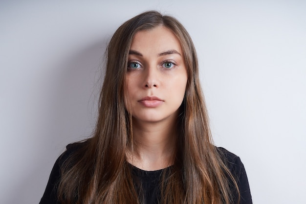 Portret van een jonge ernstige vrouw in een zwart shirt, op een grijze achtergrond