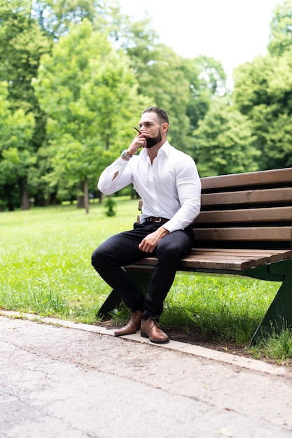 Portret van een jonge fysiek fitte zakenman die een Cubaanse sigaar rookt in het park