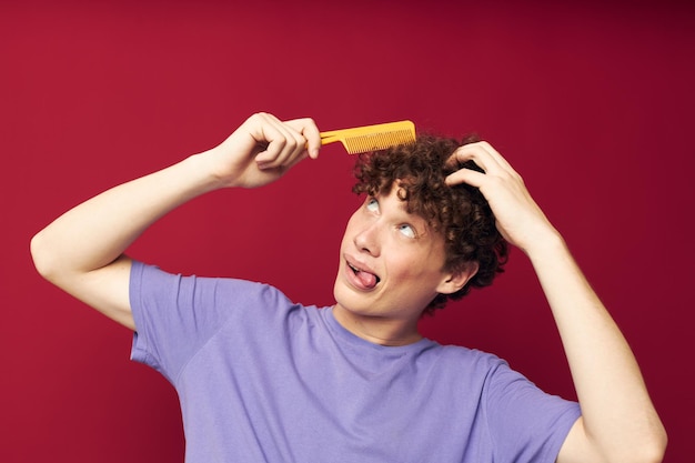 Portret van een jonge gekrulde man in paarse t-shirts met een kam geïsoleerd background