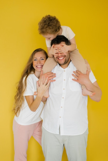 Portret van een jonge gelukkige familie ouders knuffelen een kind zoon zittend op papa's nek op een gele achtergrond Het concept van oprechte emoties