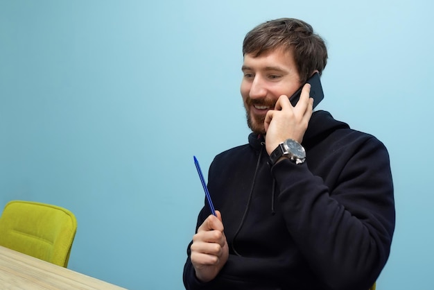 Portret van een jonge, gelukkige man die aan de telefoon praat op kantoor aan de bureautafel