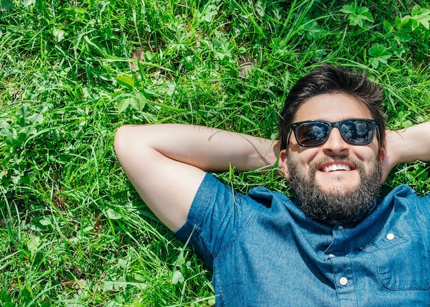 Portret van een jonge, gelukkige man die ontspant op het gras met zijn handen achter het hoofd